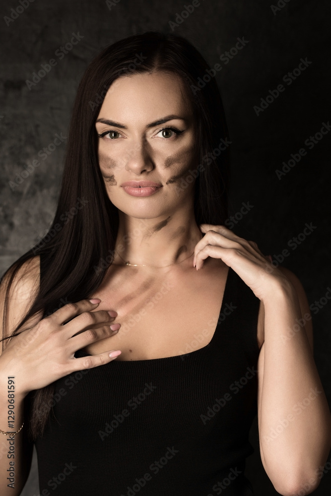 Beautiful woman in a black tank top applying camouflage military makeup to her body