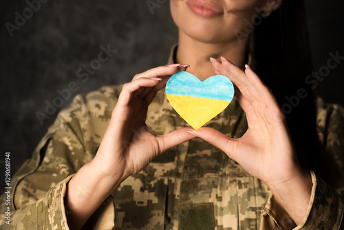 Obraz na płótnie Military woman in military uniform with camouflage makeup on her face holds a heart-shaped Ukrainian flag in her hands. Close-up w salonie