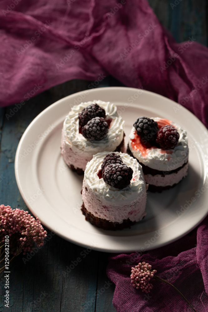Delicious cream cakes with frozen blackberries on a white plate, top view