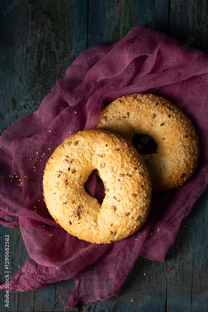 Homemade large bagels with sesame, flax and sunflower seeds on burgundy gauze, top view