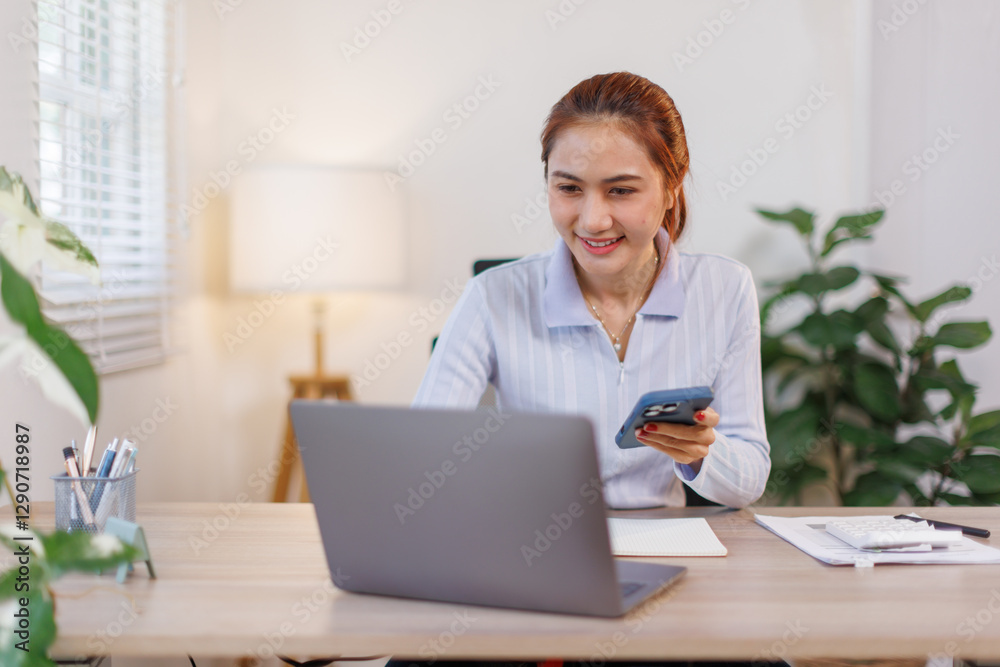 Serious charming asian woman using smartphone while working with laptop at home workplace.
Serious charming asian woman using smartphone while working with laptop at home workplace.