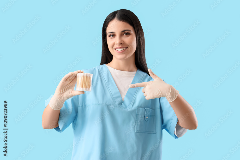 Female doctor pointing at cotton buds on blue background Female doctor pointing at cotton buds on blue background