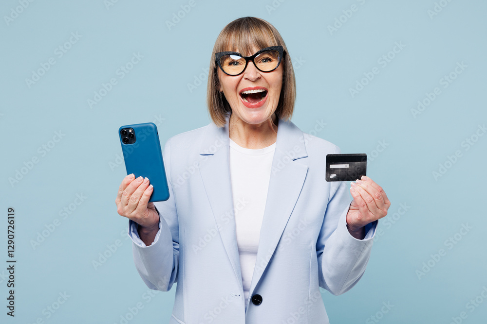 Employee business woman 50s wear classic suit glasses formal clothes use mobile cell phone hold credit bank card shopping online booking tour isolated on plain blue background. Lifestyle work concept. Employee business woman 50s wear classic suit glasses formal clothes use mobile cell phone hold credit bank card shopping online booking tour isolated on plain blue background. Lifestyle work concept.