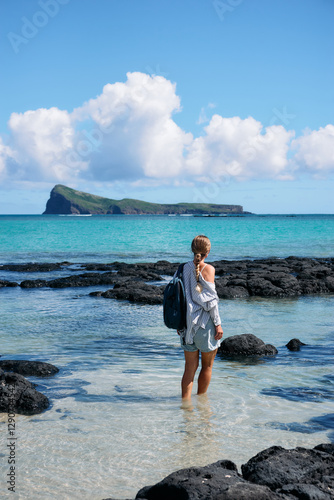 A young woman strolls along a stunning beach with a view of the iconic Coin de Mire Island, Mauritius