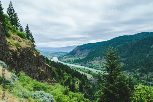 A scenic view of a river winding through lush green hills and forests under a cloudy sky.