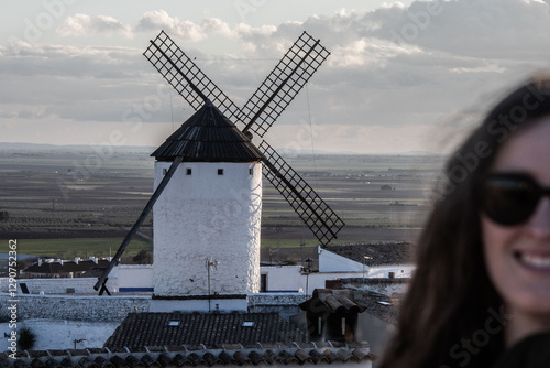 Un molino de viento tradicional de Castilla-La Mancha se alza sobre el paisaje urbano bajo una luz suave, evocando la historia y la cultura de la región inmortalizada en Don Quijote de la Mancha.