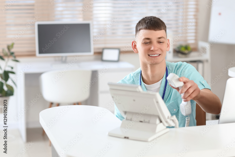 Male medical intern taking phone at reception desk in clinic
