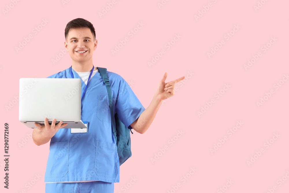 Male medical intern with laptop pointing at something on pink background Male medical intern with laptop pointing at something on pink background