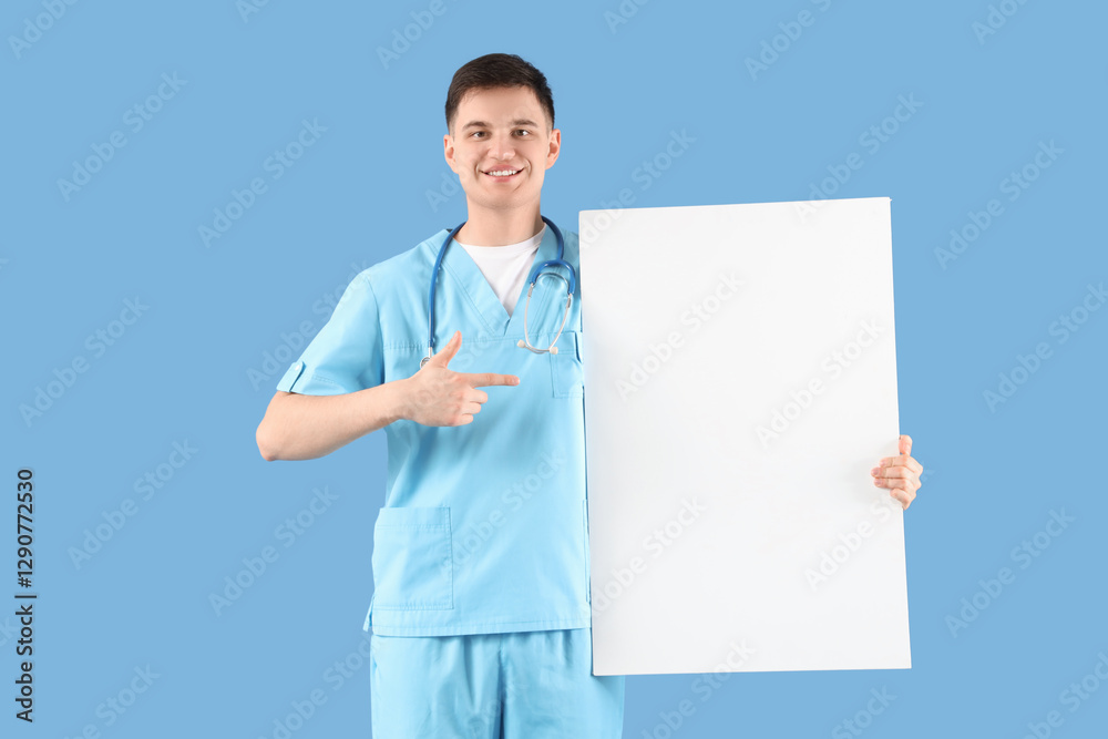 Male medical intern pointing at blank poster on blue background Male medical intern pointing at blank poster on blue background