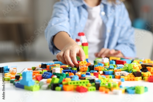 Girl playing with building blocks at white table indoors, closeup