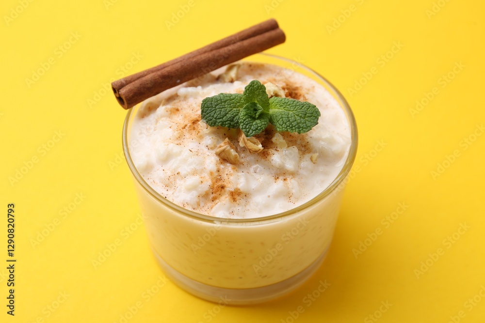 Tasty rice pudding with cinnamon, mint and nuts in glass bowl on yellow background, closeup Tasty rice pudding with cinnamon, mint and nuts in glass bowl on yellow background, closeup