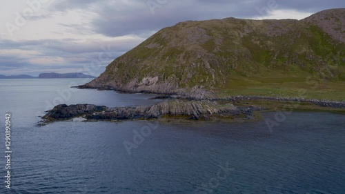 Dark, rugged rocks jut out into a bay in Norway, aerial view.