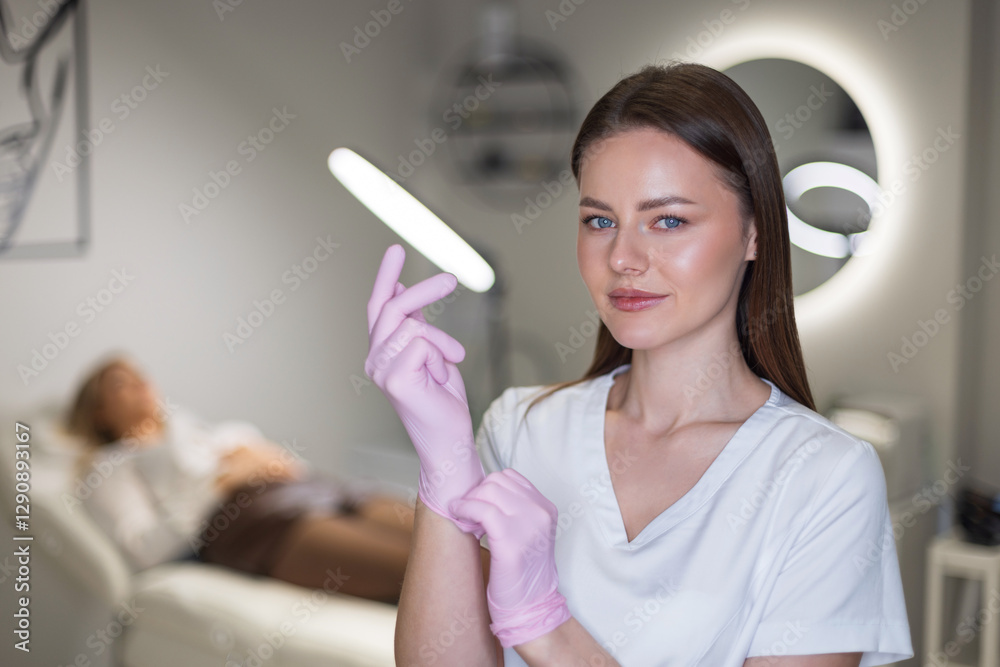 Beautiful cosmetologist happy doctor woman putting on pink gloves before procedures in white coat in beauty clinic. Professional girl Beautiful cosmetologist happy doctor woman putting on pink gloves before procedures in white coat in beauty clinic. Professional girl