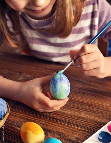 Little girl painting easter egg on old wooden table photo