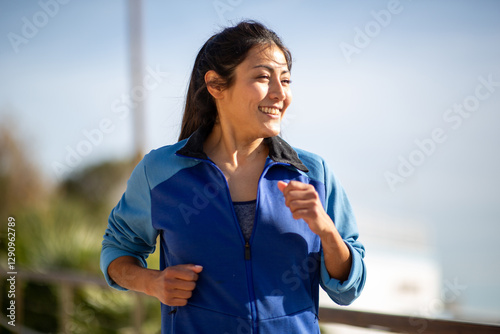 Young mixed raced woman jogging outdoors in a blue sports jacket