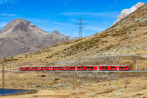 Samedan, Switzerland - 31 October 2024: View of the scenic Bernina Express train traveling through beautiful alpine landscapes with mountains and meadows, Samedan, Switzerland.