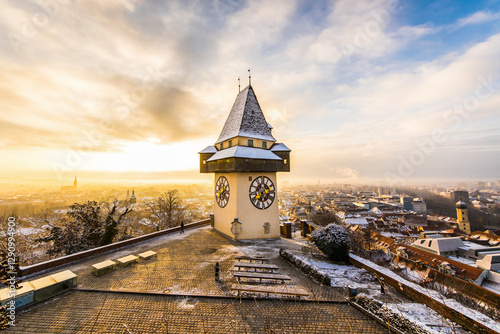 View of winter cityscape with uhrturm clocktower at sunrise surrounded by snowy rooftops, Graz, Austria. photo