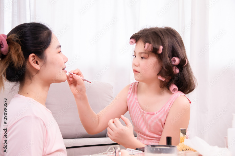 Cheerful young girl with pink curlers in her hair shares loving moment with her mother, enjoying fun and affectionate beauty routine at home. Take turns applying makeup, family warmth, spending time. Cheerful young girl with pink curlers in her hair shares loving moment with her mother, enjoying fun and affectionate beauty routine at home. Take turns applying makeup, family warmth, spending time.