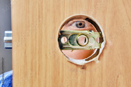 Latch plate aligns within bore hole of wood door, exposing human eye peering through opening, alongside visible mortise hardware awaiting installation.