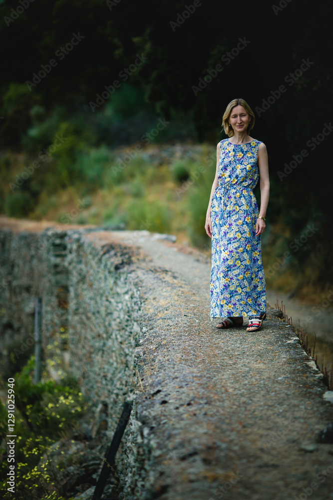 A woman in a light dress walking along a stone wall in a vineyard. The Douro Valley, Portugal.