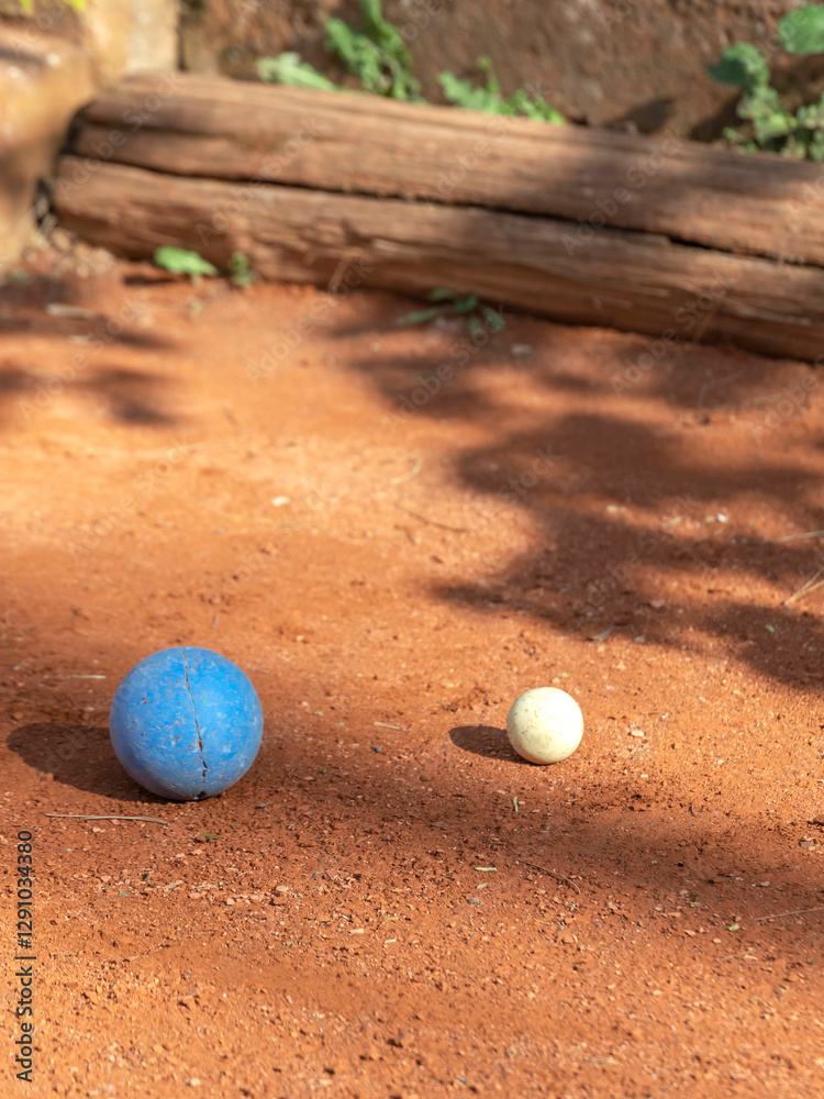 Two small balls, one blue and one yellow, are sitting on a dirt field