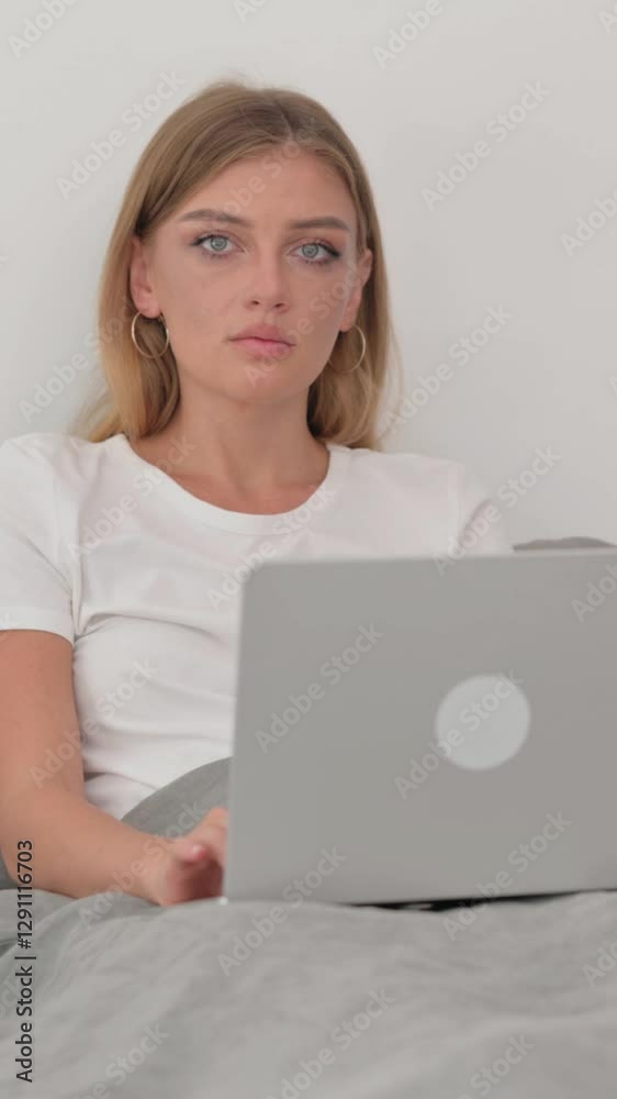 Serious Young Woman Looking at Camera while in Bed with Laptop Serious Young Woman Looking at Camera while in Bed with Laptop