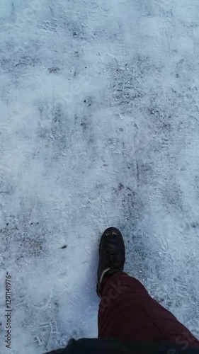 First-person top-down view of the winter walk on snowy ground. Female legs in brown boots stomp on icy track. Vertical 4k video, 26 seconds. Perfect for winter, cold weather, or outdoor content