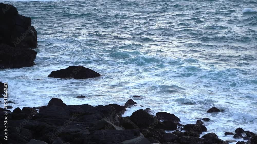 Steady shot of the cold frothy Atlantic ocean waves splashing against the rocky shore of an Icelandic black beach Steady shot of the cold frothy Atlantic ocean waves splashing against the rocky shore of an Icelandic black beach