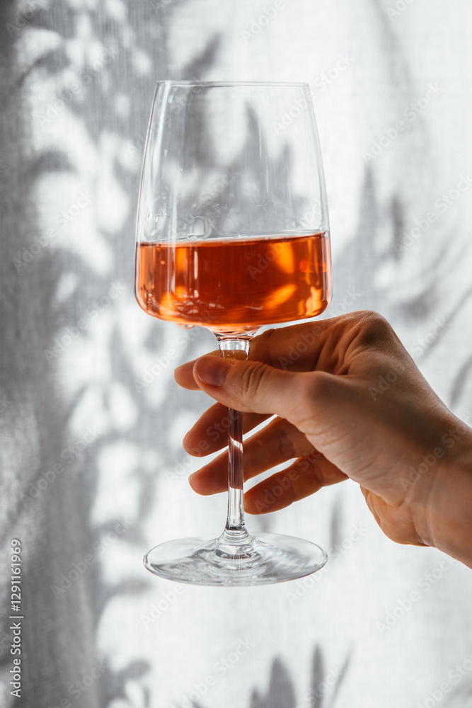 Hand holding a glass of rose wine in summer sunshine during a wine tasting in a bar or restaurant.