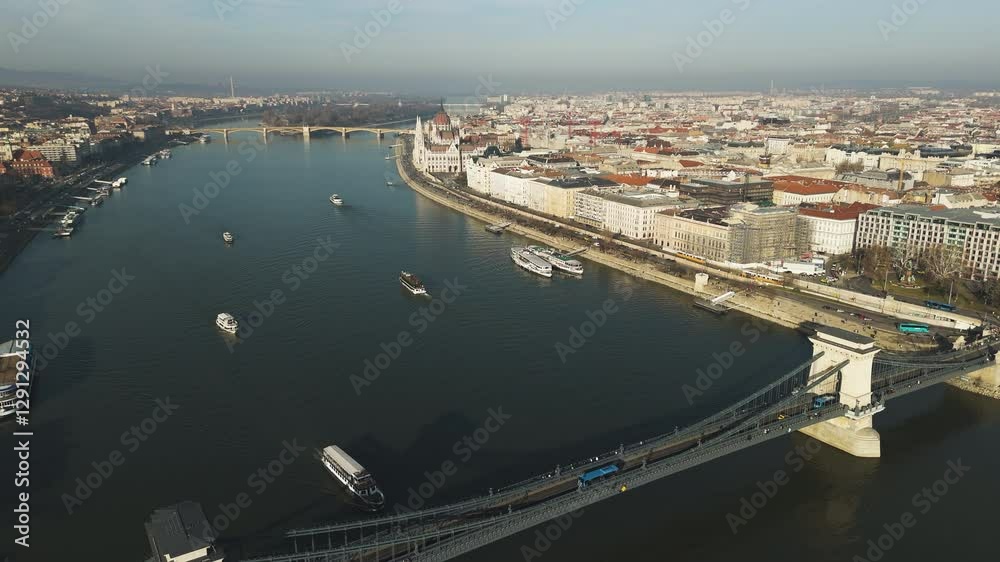 Aerial pullback over chain bridge in Budapest, Hungary, the Danube River and historic architecture during golden hour as ferries drive along Aerial pullback over chain bridge in Budapest, Hungary, the Danube River and historic architecture during golden hour as ferries drive along