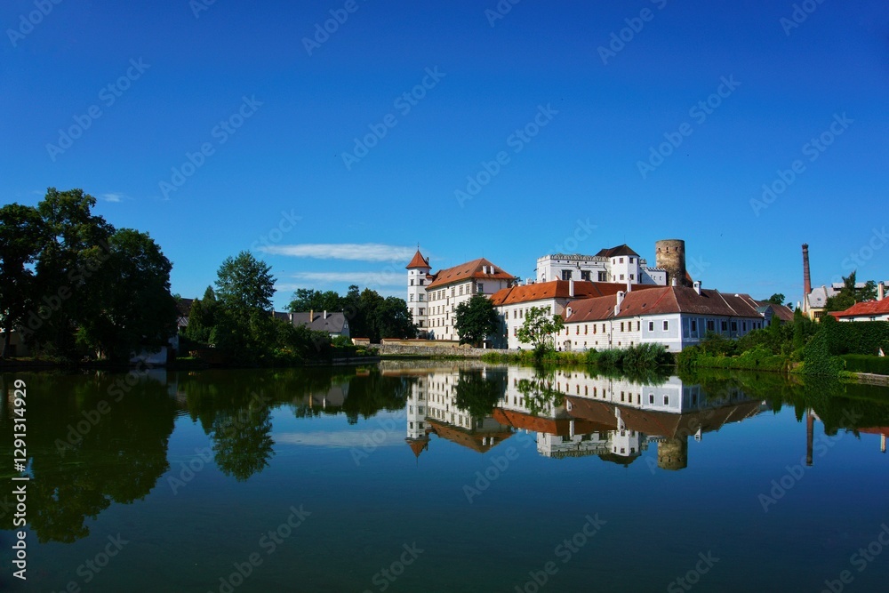 A serene view of Jindřichův Hradec Castle in the Czech Republic, reflecting beautifully in the calm waters of the pond. The castle's white walls and red rooftops stand out against the clear blue sky. A serene view of Jindřichův Hradec Castle in the Czech Republic, reflecting beautifully in the calm waters of the pond. The castle's white walls and red rooftops stand out against the clear blue sky.