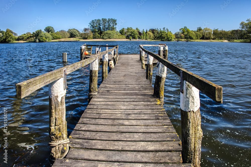 Long wooden pier stretching into a serene lake on sunny day Long wooden pier stretching into a serene lake on sunny day
