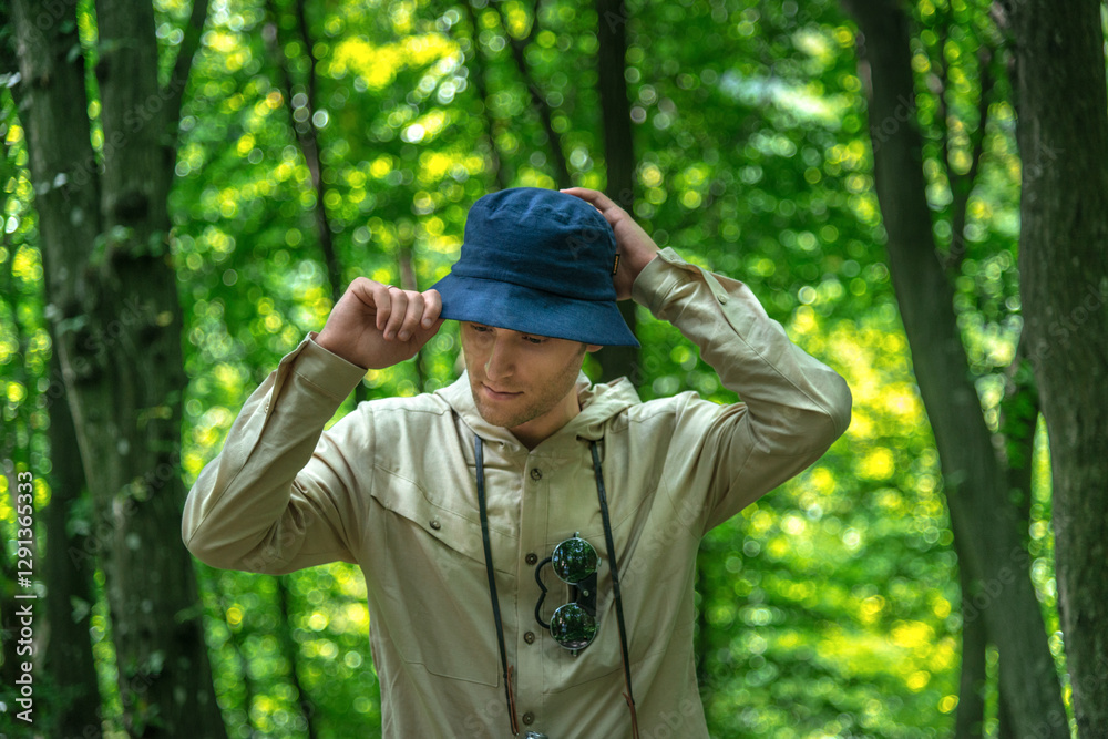 Young man putting on hat amidst a backdrop of captivating forest scenery exploring forest during spring or summer Young man putting on hat amidst a backdrop of captivating forest scenery exploring forest during spring or summer