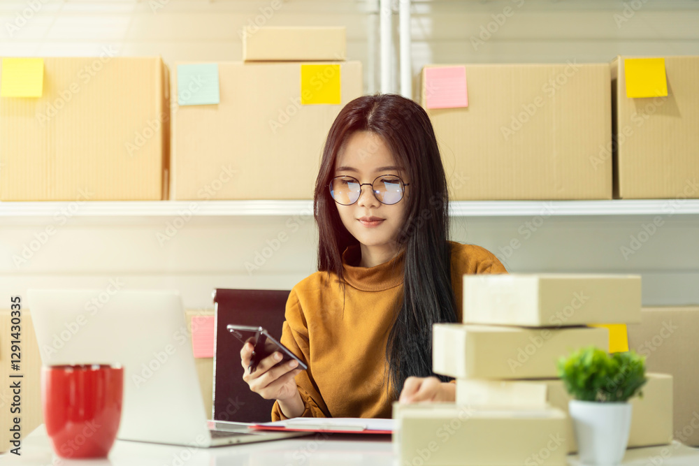 Asian owner holding a smartphone. Female entrepreneur preparing orders for shipping in a warehouse. Businesswoman running an e-commerce small business. Asian owner holding a smartphone. Female entrepreneur preparing orders for shipping in a warehouse. Businesswoman running an e-commerce small business.