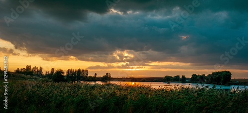 Panorama of a sunset over a lake or river. Dark clouds over the lake, creatin...