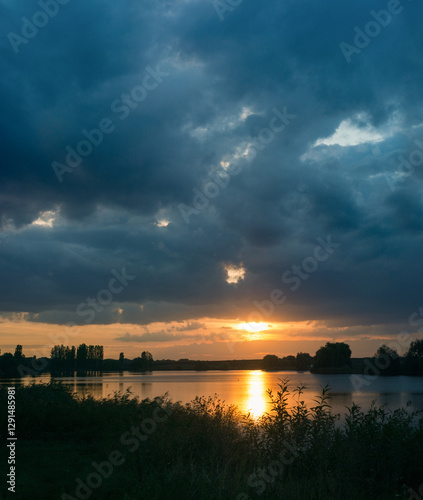 beautiful sunset, warm rays break through dark clouds over the lake and the s...