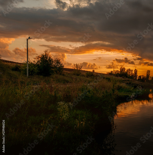 silhouettes of a pillar, trees on the shore of a lake, sunset, reflection in ...