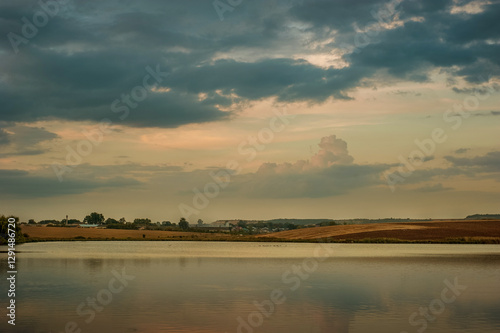 landscape of a calm pond and evening sky, view of fields on the opposite bank...