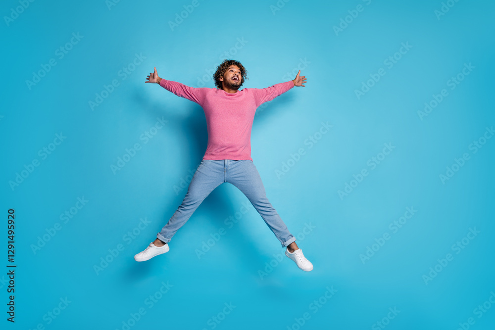 Joyful young man jumping with enthusiasm in a vibrant pink outfit against a bright blue background Joyful young man jumping with enthusiasm in a vibrant pink outfit against a bright blue background