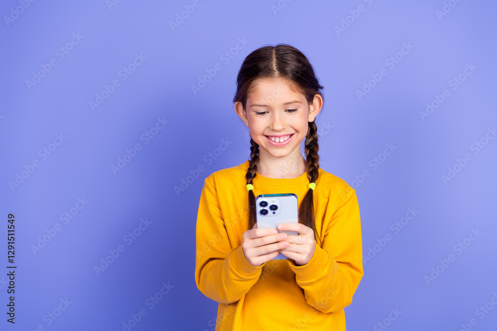 Smiling young girl using a smartphone against a vibrant violet wall, looking cheerful and trendy in orange sweatshirt Smiling young girl using a smartphone against a vibrant violet wall, looking cheerful and trendy in orange sweatshirt