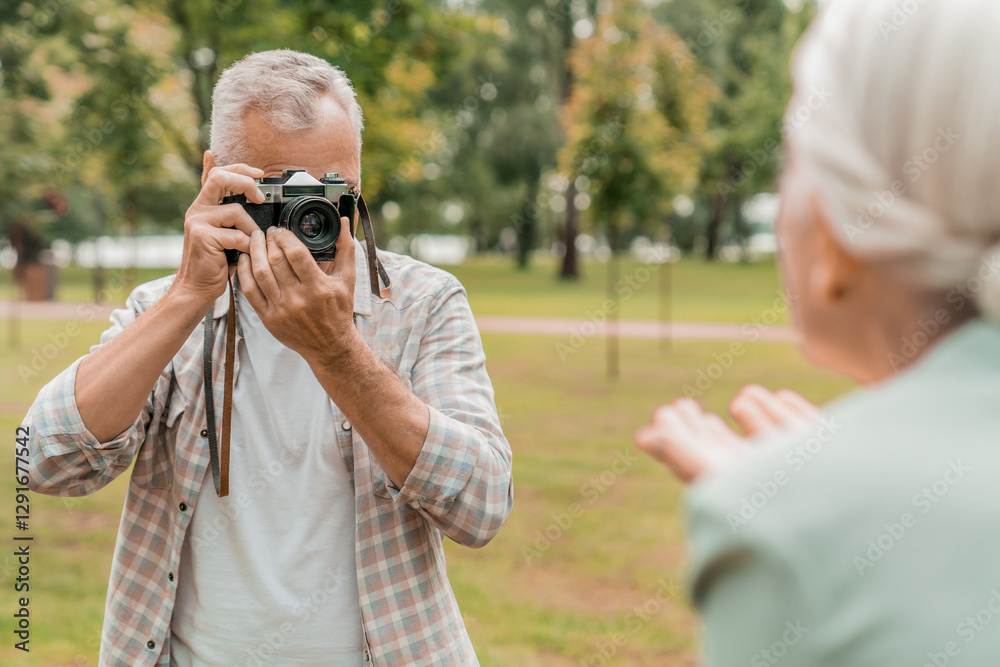 Handsome old elderly man photographing his wife by photo camera outside. Senior couple in park spend time together. Retirement insurance and lovely couple concept Handsome old elderly man photographing his wife by photo camera outside. Senior couple in park spend time together. Retirement insurance and lovely couple concept