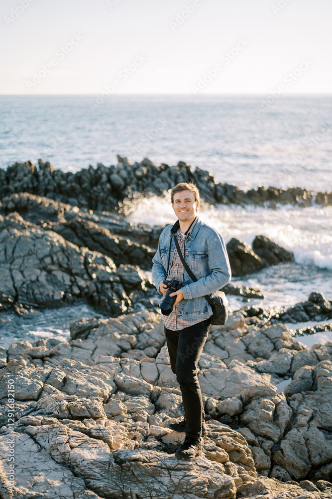 Obraz premium Smiling photographer with a digital camera in his hands stands on a rocky seashore