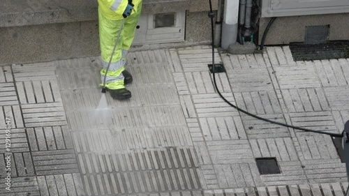 Street cleaner is using a pressure washer to clean a city sidewalk