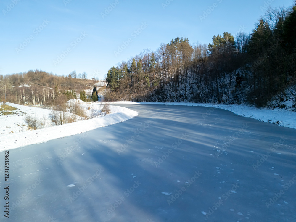 Obraz premium A serene winter landscape featuring a winding frozen river surrounded by snow-covered trees under a clear blue sky
