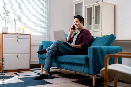 Asian Freelancer Talking on Phone and Working on Laptop at Home