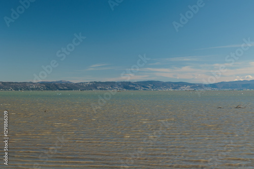 Obraz na płótnie vista che si estende sull'area marina del Golfo di Trieste, nel mare Adriatico, guardando verso le colline e le montagne distanti tra Italia e Slovenia, di giorno, con cielo sereno, in inverno w salonie