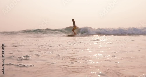 Sexy surfer on surfboard rides on ocean wave in morning with warm sunlight. Surfing woman riding on longboard.
