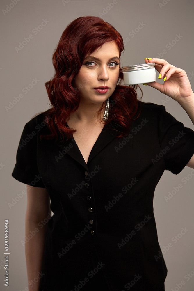 Woman holding cosmetic jar with red hair, black outfit, striking pose, expressing beauty, elegance, focus on skincare product, beauty care concept