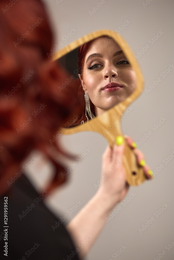 Reflection of woman with red hair, green nails holding wooden mirror, elegant makeup, chandelier earrings, beauty concept