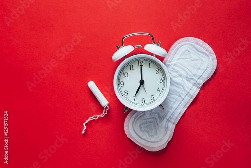 Hygienic female pad with tampon and alarm clock on red background, flat lay. photo